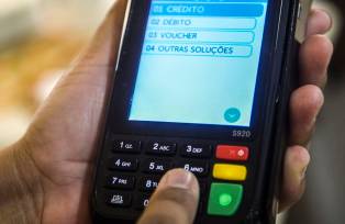 Máquina de cartão crédito e débito na mão de uma pessoa clicando no botão